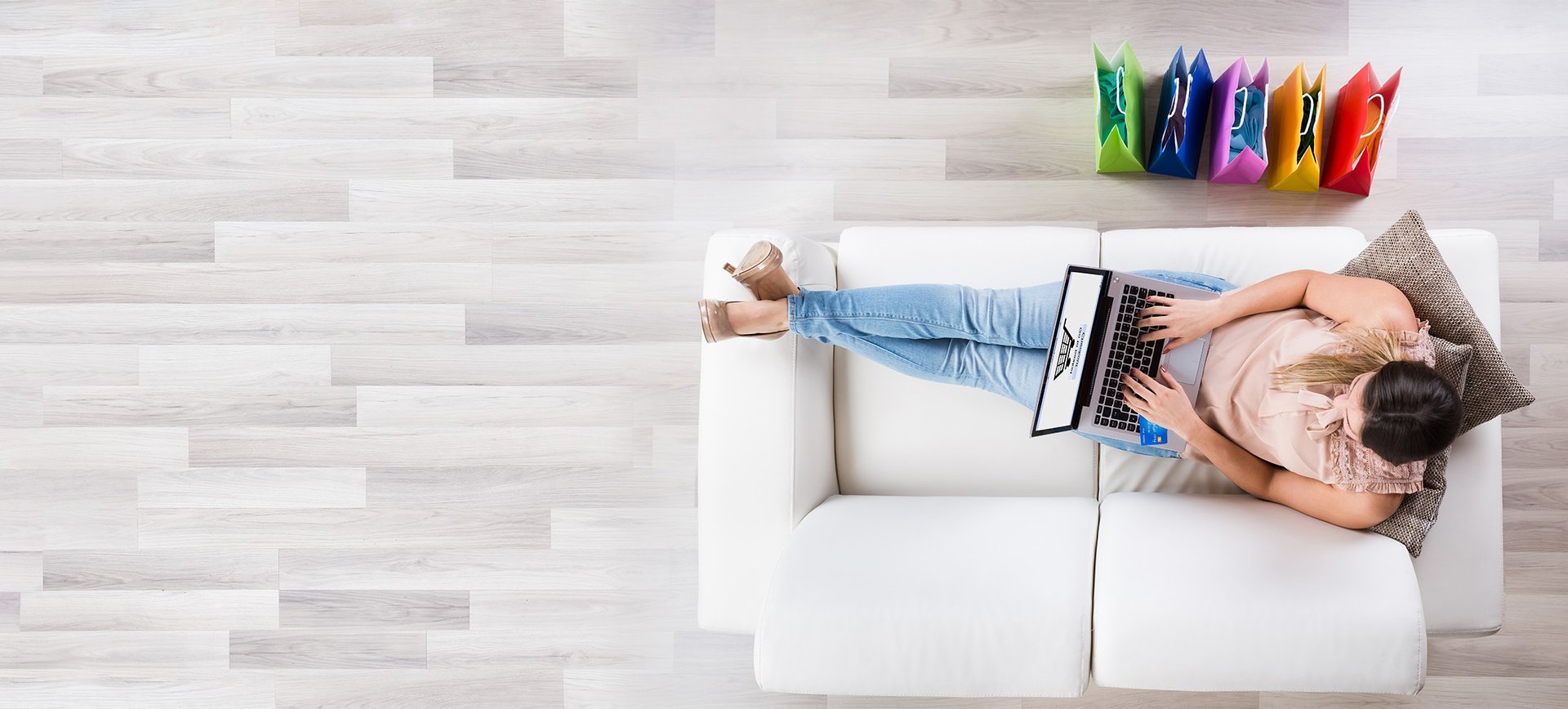 Eine Frau sitzt auf einem weißen Sofa und kauft über ihren Laptop in einem Online-Shop ein.