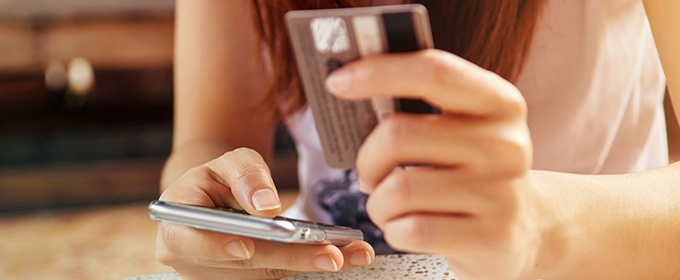 Eine Person kauft online über ihr Smartphone ein. In der freien Hand hält sie eine Kreditkarte.