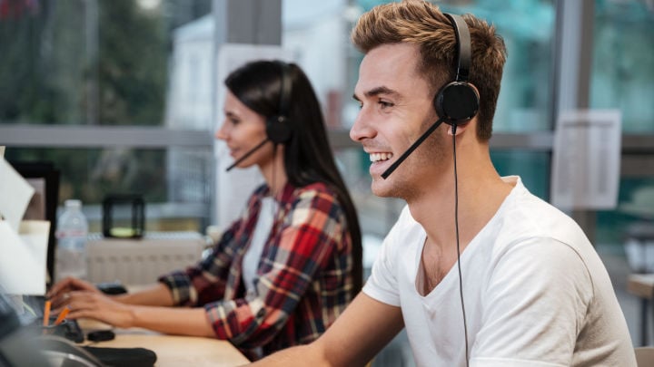 Kundenservice: Zwei lächelnde Call-Center-Mitarbeitende sitzen an einem Tisch mit Headsets.