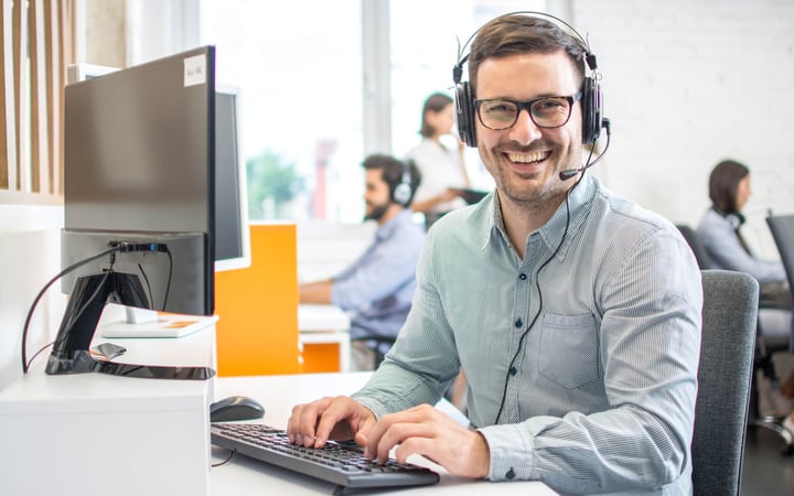 Ein Kundenservice-Mitarbeiter sitzt vor seinem PC und trägt ein Headphone.