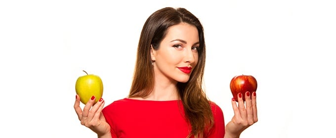 Eine Frau hält in einer Hand einen grünen und in der anderen Hand einen roten Apfel.