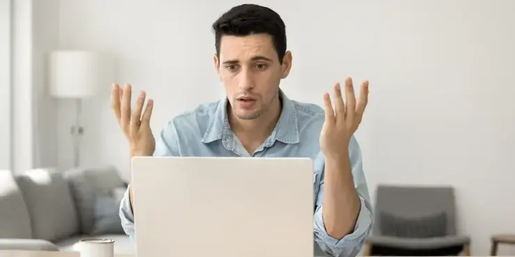 Ein junger Online-Händler schaut entsetzt in seinen Laptop.