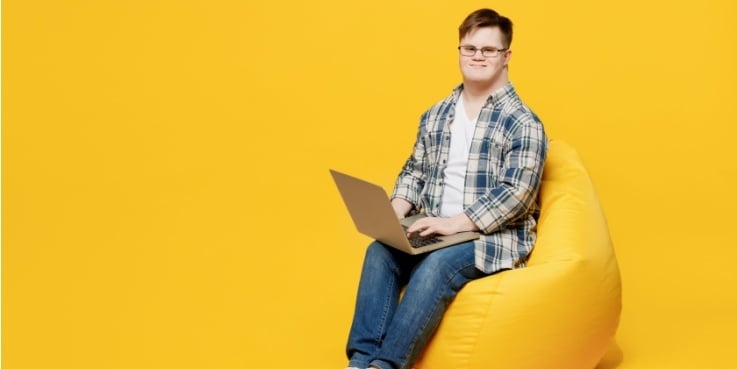 Ein junger Mann mit Down-Syndrom sitzt an einem Laptop.