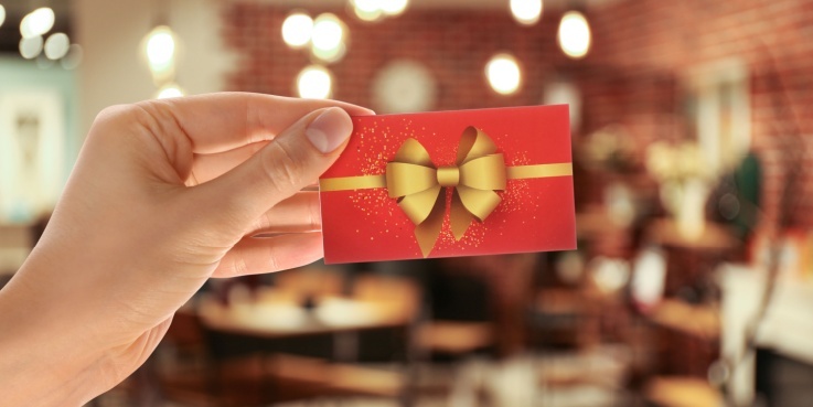 Eine Hand hält einen Geschenkgutschein hoch.