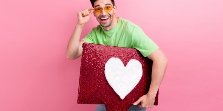 Ein junger Influencer hält ein Like-Symbol unterm Arm.