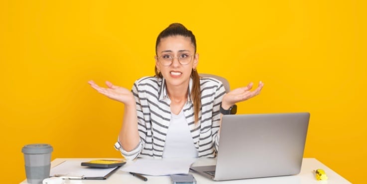 Eine Unternehmerin sitzt achselzuckend vor einem Laptop.