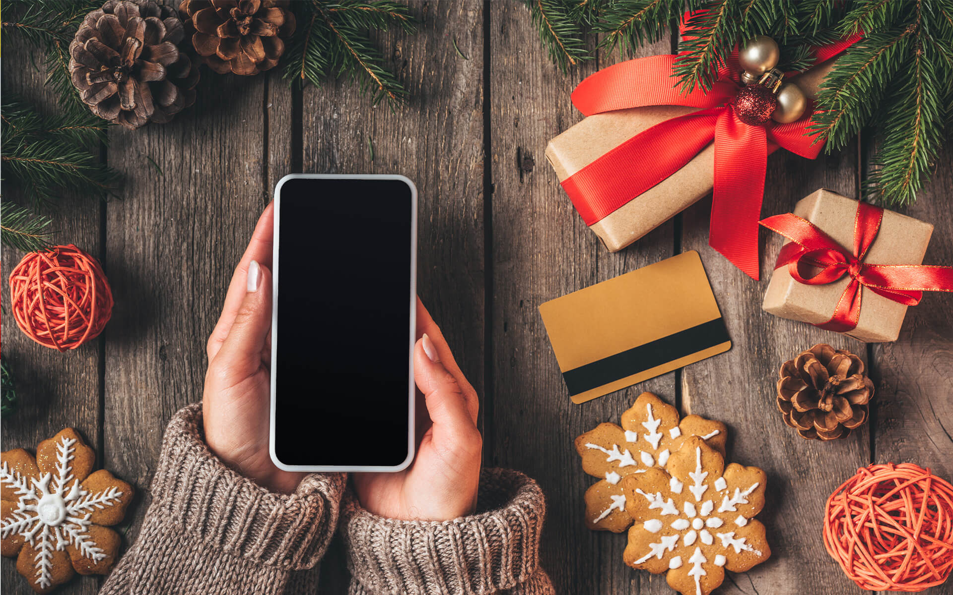 Eine Frau hält ein Smartphone in der Hand. Auf einem Tisch ist Weihnachtsdekoration zu sehen.