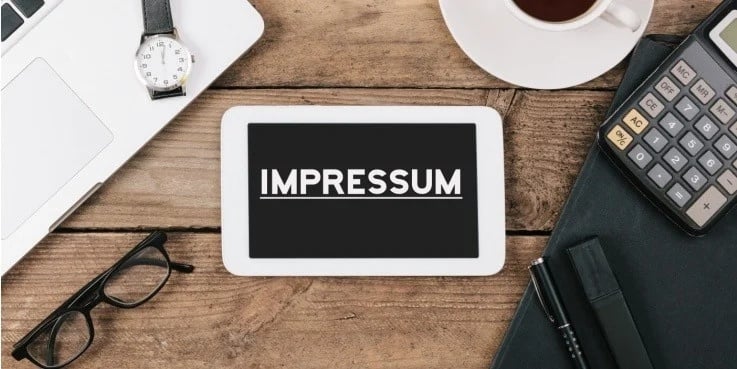 Tablet mit der Aufschrift „IMPRESSUM“ auf einem Schreibtisch mit Büroutensilien als Symbol für Impressumspflichten und rechtliche Informationen auf Websites.